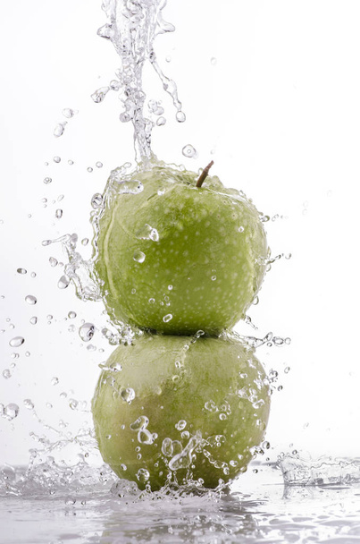 eine Welle klaren Wassers fällt auf den grünen Apfel auf weißem Hintergrund - Foto, Bild