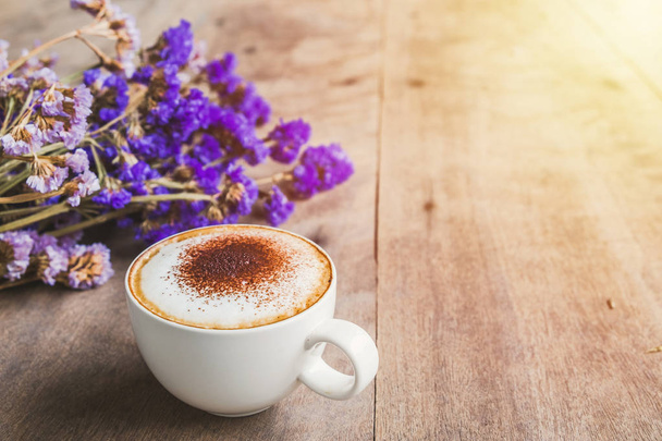 A cup of coffee with bouquet of violet dried flowers on wooden floor background,in morning sun. - Photo, Image