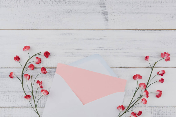 Beyaz zarf içinde boş pembe kart süslemek kopya alanı beyaz ahşap zemin üzerine kırmızı kağıt çiçeklerle - Fotoğraf, Görsel
