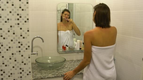 Woman brushing his teeth in front of the mirror in the bathroom - Πλάνα, βίντεο