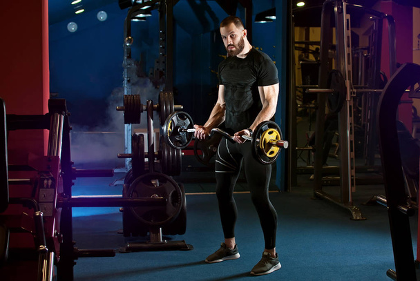 a man is training. heavy physical exercises in the gym. sports equipment. gym with blue light. - Fotografie, Obrázek
