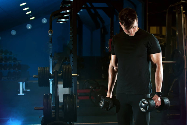 a man is training. heavy physical exercises in the gym. sports equipment. gym with blue light. - Fotografie, Obrázek