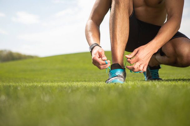 Sportsman is tying shoe laces on grass - Foto, afbeelding