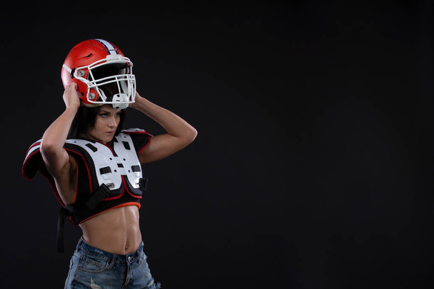 Портрет сексуальной привлекательной молодой девушки с ярким макияжем в спортивном костюме для регби со шлемом на голове, сильно смотрящим вперед, стоящим на черном фоне. гендерное равенство Копирование пространства
 - Фото, изображение