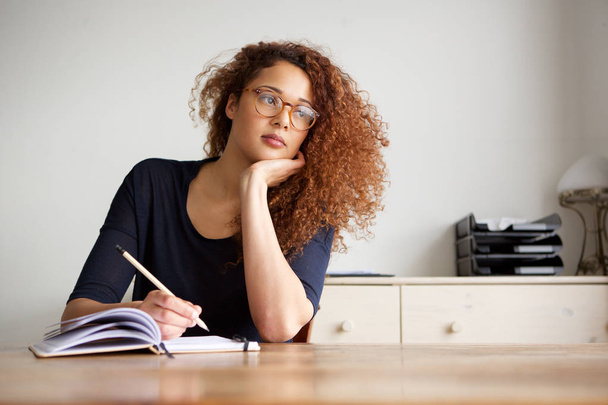 Portrait of female student sitting at desk and writing notes in book - Photo, Image