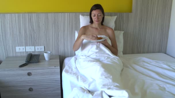 Woman drinking coffee and eating pizza lying in bed at hotel - Imágenes, Vídeo