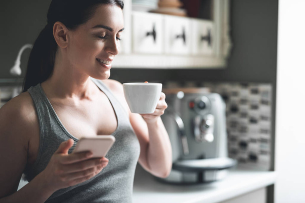 Relaxed woman drinking hot drink and using phone at home - Foto, afbeelding