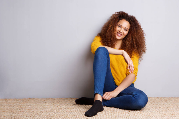 Portrait de fille afro-américaine assise sur le sol et souriant par un mur gris
 - Photo, image