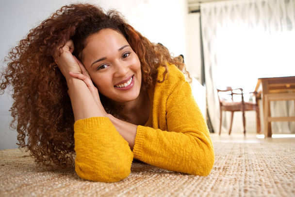 Portret van Afro-Amerikaanse meisje met krullend haar op vloer thuis liggen - Foto, afbeelding