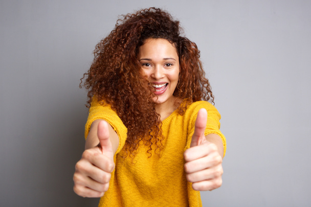 Портрет веселої молодої жінки з великими пальцями на сірому фоні
 - Фото, зображення