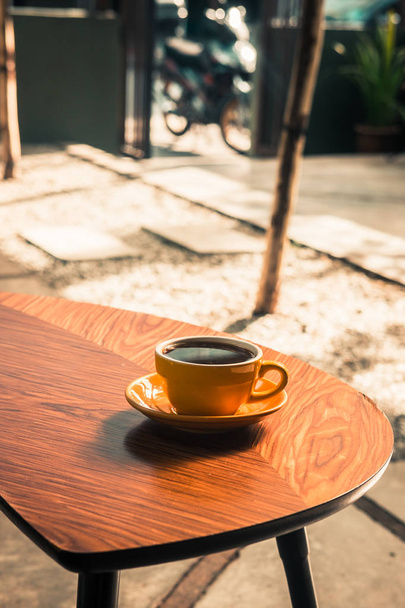 Erikoisuus suodatin kahvia keltainen kuppi puinen pöytä hipster kahvila. Auringonvaloa. Vintage väri suodatin vaikutus. Copyspace; pystysuora - Valokuva, kuva