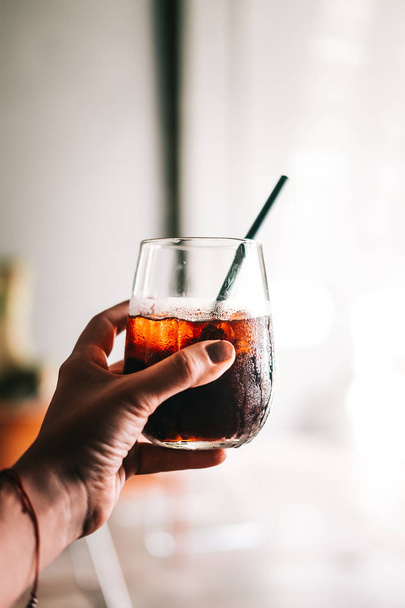 Woman's hand holding glass of black cold brew coffee with ice. Hipster coffee shop. Minimalism drink photography - Photo, Image