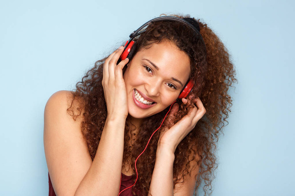 Porträt einer fröhlichen jungen Frau, die vor blauem Hintergrund mit Kopfhörern Musik hört - Foto, Bild