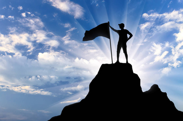 Silhouette of a climber with a flag on top of a mountain. Conceptual scene of success - Photo, Image