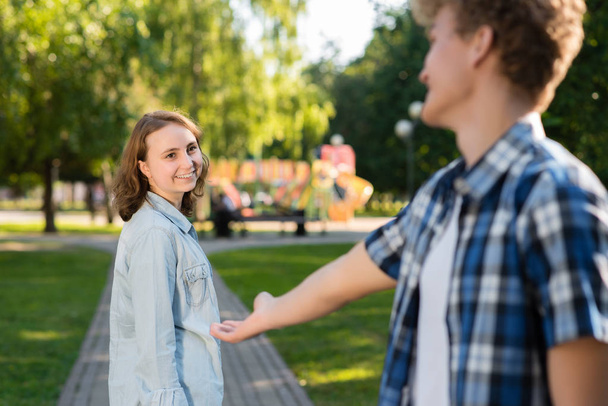In the summer in park in nature. The young man gets acquainted with the girl. She stretches out her hand for communication. The girl smiles happily says yes. Dating in the city. - 写真・画像