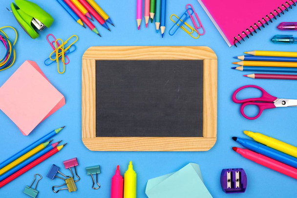 Blank chalkboard with school supplies frame against a soft blue paper background. Copy space. - Foto, Imagem