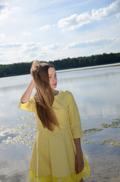 Uma mulher pequena no lago. Modelo feminino com vestido amarelo em pé perto da água
. - Foto, Imagem
