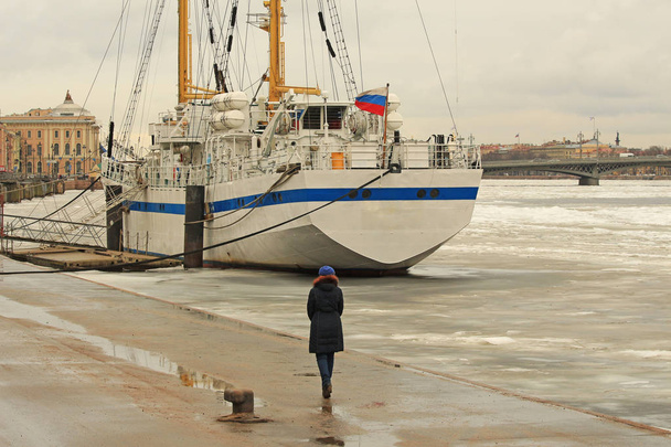 una donna che cammina lungo l'argine invernale vicino a una barca a vela ghiacciata
 - Foto, immagini