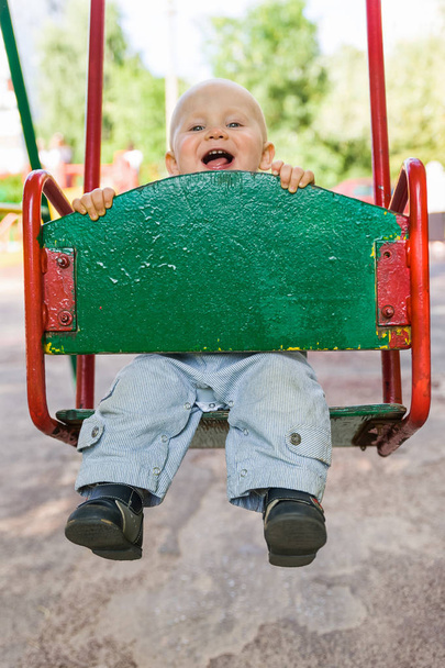 little boy swinging on a swing with a smile and tongue sticking out - Фото, зображення