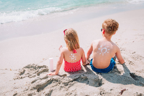 защита от солнца - мальчик и девочка с солнцезащитным кремом на пляже
 - Фото, изображение