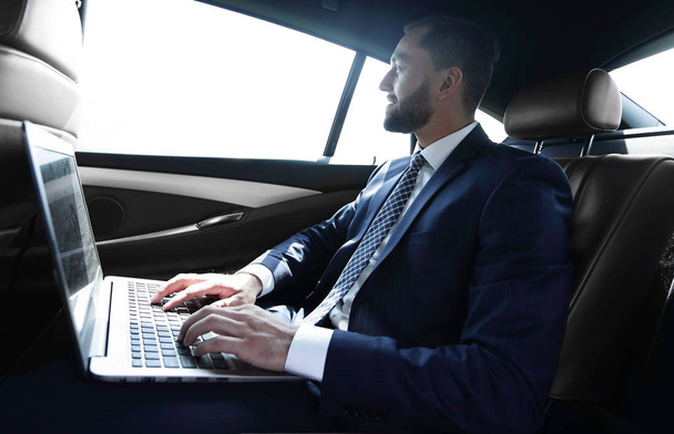 Businessman typing text on laptop while sitting in car - Photo, image