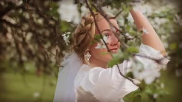 Chica joven en una túnica blanca contra el telón de fondo de un jardín de primavera
. - Metraje, vídeo