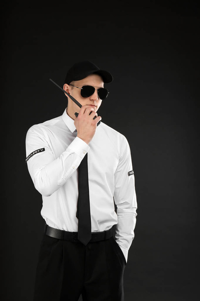 Male security guard using portable radio transmitter on dark background - Foto, afbeelding