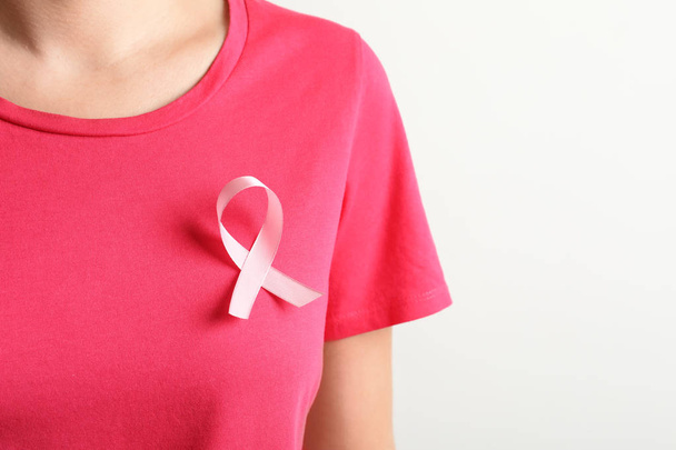 Woman with pink ribbon on t-shirt against light background. Cancer awareness - Foto, Imagem
