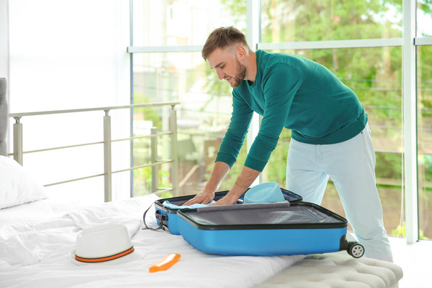 Young man packing suitcase for summer journey on bed - 写真・画像