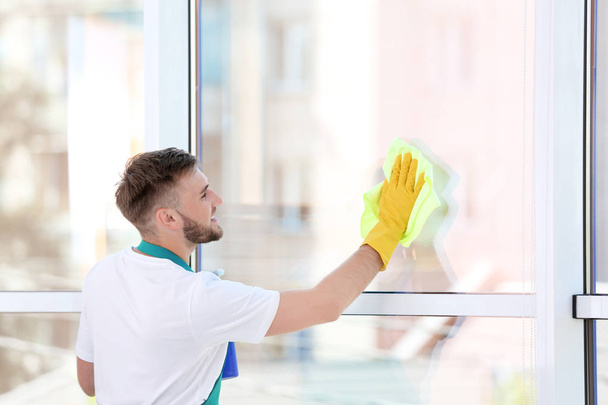 Young man cleaning window with rag indoors - Fotoğraf, Görsel