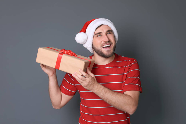 Young man with Christmas gift on grey background - Fotó, kép