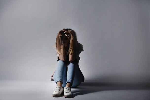 Osamělá depresivní žena sedící na šedém pozadí - Fotografie, Obrázek