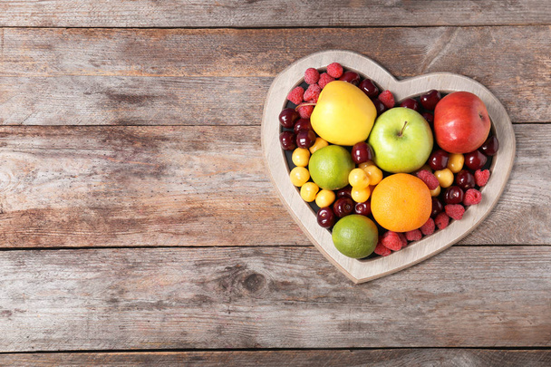Heart shaped plate with fresh fruits on wooden table, top view. Cardiac diet - Fotoğraf, Görsel