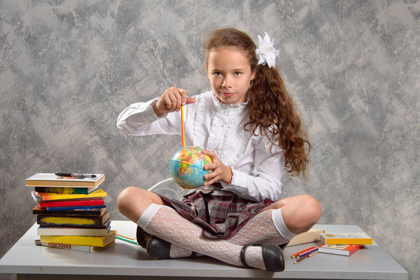 The fidget schoolgirl in school uniform sits on table and smiles happily on a light gray background. Back to school. The new school year. Child education concept. - Photo, image