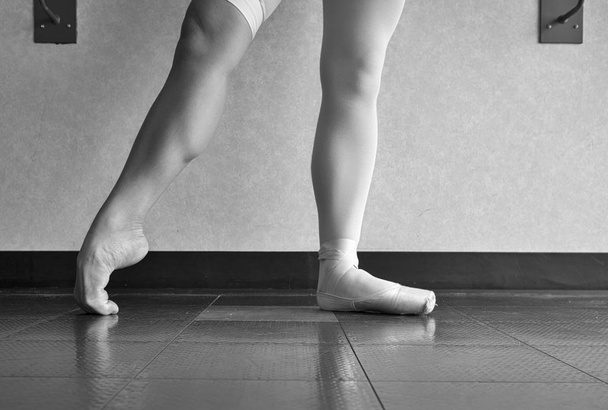 Schwarz-weiße Version der fleißigen disziplinierten Ballerina-Balletttänzerin, die sich in ihren Spitzenschuhen und barfüßigen Füßen aufwärmt und den Blick hinter die Kulissen einer Tänzerin zeigt - Foto, Bild