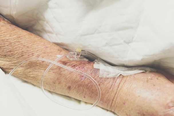 Pacjenta starszy Azjatek 80s soli fizjologicznej podany dożylnie w C-linia lub linia a na pacjenta w podeszłym wieku z ręką na łóżku pacjenta łóżko w sali intensywnej terapii (OIT.) w szpitalu. - Zdjęcie, obraz