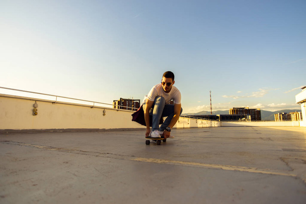 Cool τύπος με ένα skateboard το ηλιοβασίλεμα σε μια ταράτσα στο ηλιοβασίλεμα - Φωτογραφία, εικόνα