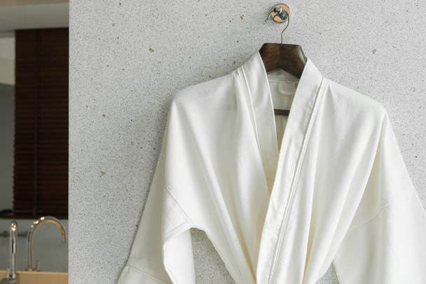 White bathrobe on a hanger on the wall by the window in the bathroom. - Photo, Image