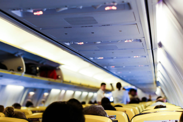 Wazig foto van interieur van vliegtuig en passagiers met zakken op de planken. - Foto, afbeelding
