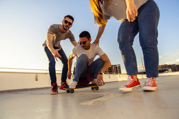 Adolescente ativo montando longboard com seus amigos no telhado do edifício
 - Foto, Imagem