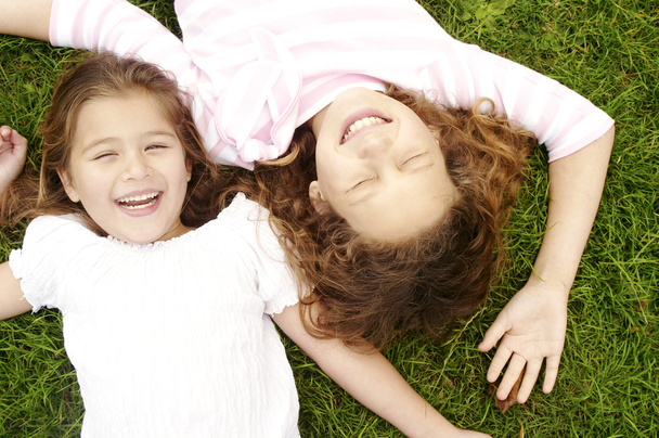 napowietrznych portret dwóch dziewczynek ustanawiające na zielonej trawie, śmiejąc się. - Zdjęcie, obraz