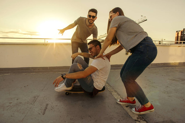 Adult friends on terrace having fun while driving skateboard - Photo, Image