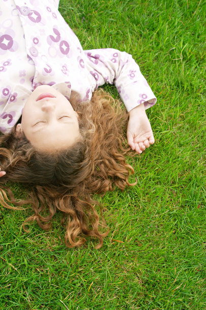 über dem Kopf eines jungen Mädchens, das sich mit geschlossenen Augen auf das grüne Gras legt. - Foto, Bild