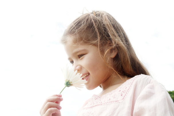 Young girl smelling white daisy flower against the sky, smiling. - Foto, Bild