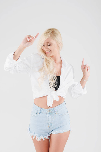 Young happy and positive blonde girl with long hair is having fun and waving her hands on a white isolated background. Model dances and laughs - Fotografie, Obrázek