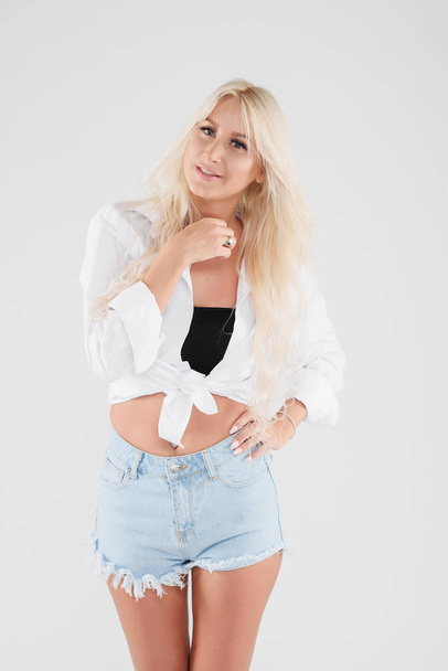 Portrait of a young slender female model in summer clothes, shorts and a shirt on a white isolated background. Carefree happy sunburnt girl - Foto, Imagen