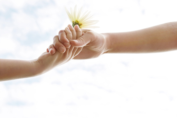 花を保持しながら、空に抱かれている二人の若い女の子の手. - 写真・画像