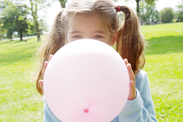 Jovencita inflando un globo rosa frente a su cara en el parque en un día soleado
. - Foto, imagen