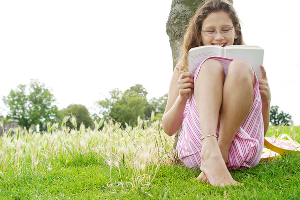 Jovencita leyendo un libro sentado bajo un árbol en el parque
. - Foto, imagen