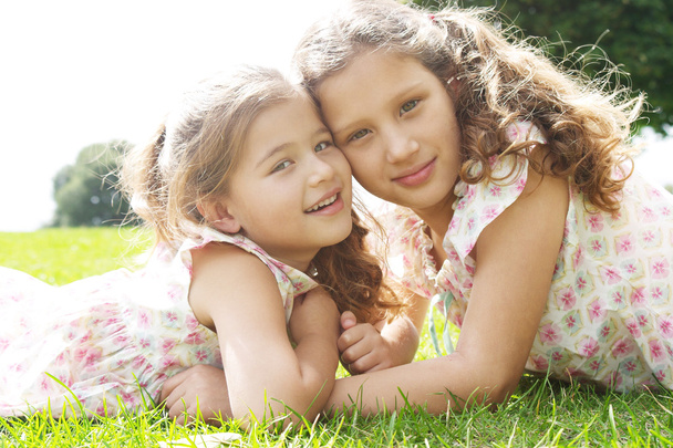 dwie siostry ustanawiające na zielonej trawie w parku - Zdjęcie, obraz